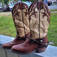 Side profile view of the full pair of two-tone leather riding boots with attached spurs showing their shape and wear.