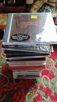 Stack of 24 brand new, unopened CDs with visible album covers including The Carpenters.