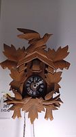 Front view of wooden cuckoo clock with carved bird on top and leaves around the clock face showing Roman numerals.