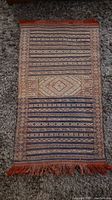 Full view of the hand knotted rug laid flat on a carpeted floor showing geometric medallion and linear stripe patterns.