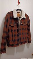 Full frontal image of the brown and black plaid Levi's jacket with sherpa lining, hung on a hanger showing overall garment condition and design.
