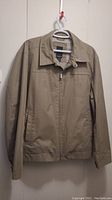 Front view of beige London Fog men's jacket with zipper closed, displayed hanging on a hanger.