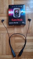 Boxed SanDisk Sansa Clip Zip MP3 player in original packaging with Skullcandy earbuds placed beside the box on wooden floor.