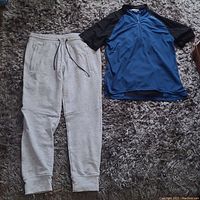 Pair of light grey American Eagle sweat pants alongside blue and black Sugoi biking shirt on carpeted surface