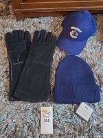 Lot items on carpet showing black grilling gloves, navy Vancouver Canucks cap, and indigo knit tuque with product tag.