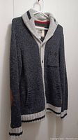 Front view of dark grey textured knit cardigan with light grey hood, button closure, and striped ribbed cuffs and hem