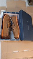 Pair of brown Tommy Hilfiger boat shoes in original box showing side view and box with brand name.