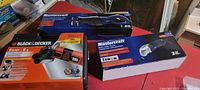 Photo of three boxed power tools: Black & Decker angle grinder, Mastercraft reciprocating saw, and Mastercraft multi-crafter tool kit on a red surface.