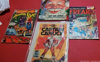 Lot of 4 vintage comic books on red surface: Inferior Five, Mad Stocking Stuffer, sealed Captain Canuck, and Fabulous Furry Freak Brothers