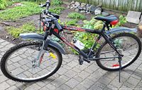 Side view of black men's mountain bike with red/white details, knobby tires, front suspension, black fenders, water bottle on frame.