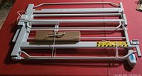 Folded white adjustable metal dog gate laid flat on red surface, including attached mounting hardware and instructions in a box.