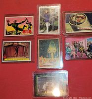 Overview of 7 assorted collectible cards in protective sleeves on a red surface