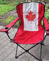 Front view of red folding camping chair with Canada flag on backrest and black metal frame.