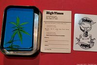 Playing cards with blue back featuring green cannabis leaf in metal tin, subscription card and illustrated card visible