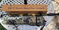 Periscope with camouflage case and original box on white outdoor table.