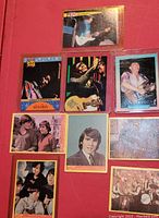 Nine assorted rock star collector cards spread out on red background, showing close up of Jimi Hendrix, Eric Clapton, Stevie Ray Vaughan and The Beatles among others.