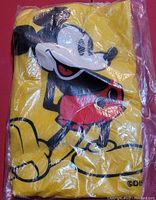 Photo of unopened vintage yellow rain poncho with large Mickey Mouse print visible through clear packaging, showing mint condition.