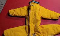 Full view of the bright yellow winter dog jacket laid flat, showing long sleeves and zipper closure.