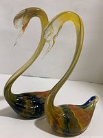 Two signed art glass swans with converging necks and colorful translucent bodies.