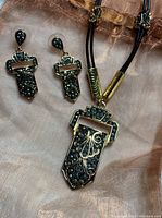 Full view of Butler marcasite pendant necklace on faux leather cord with matching earrings on a fabric background