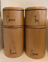 Four vintage Cornwall USA kitchen canisters with wooden exteriors, labeled Coffee, Tea, Flour, Sugar.