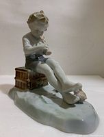 Side view of Metzler & Ortloff porcelain figurine showing boy sitting on books playing flute with three ducks nearby on base