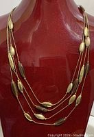 Four strand brown and gold tone Monet necklace displayed on bust showing flat serpentine link chain and hammered satin accent beads.
