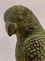 Close-up image showing detailed feather texture and painted green and gold colors on bronze/brass parrot statue.