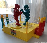 Front view showing entire yellow plastic boxing ring with two opposite facing robots (red and teal blue).
