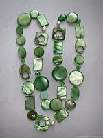 Green deco shell necklace with assorted shapes and real pearls, displayed against a gray background.