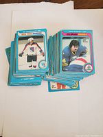 Stacks of hockey cards with front player photos visible, showing blue borders and team names (New York Rangers, Colorado Rockies)