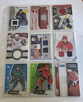 Front view of nine hockey cards, each embedded with pieces of players' jerseys in various colors, featuring different card series designs.