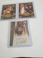 Front view of three basketball cards featuring Kobe Bryant in Lakers uniform with gold border design and Elite Series card
