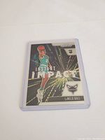 Front of LaMelo Ball rookie card showing player dunking with holographic background with 'Instant Impact' text and Hornets logo.