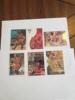 Photo showing 7 Michael Jordan basketball cards on white paper background with various designs.