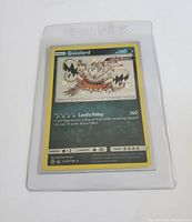 Front view of the Guzzlord Pokemon card in a plastic protective sleeve showing card details and artwork.