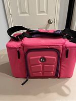 Front view of the pink fitness cooler with a front molded pocket and adjustable shoulder strap visible.