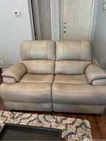 Front view showing the full beige leather love seat on wooden floor with a rug in front.