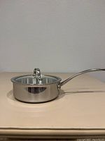 Side view of the stainless steel saucepan with lid on, showing long handle and smooth exterior surface.