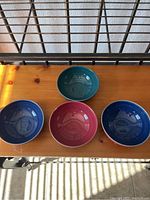 Four bowls arranged on a wooden surface: two dark blue, one red, and one green bowl.