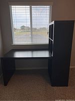 Side view of the black IKEA desk with attached vertical bookcase near a window.