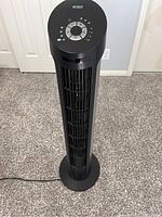 Front view of the black tower fan showing vertical grille and circular base