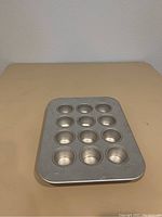 Angle view of rectangular aluminum mini cheesecake pan with 12 circular cavities, surface shows scratches and wear marks.