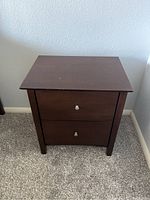 Dark brown wooden nightstand against wall, showing overall front and side profile.