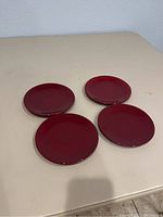 Four red Pampered Chef Simple Additions saucers arranged on table, showing overall color and condition