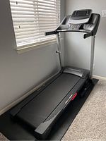 Side angle view of the PROFORM City T7 treadmill on the floor mat near a window, showing the digital screen and handrails.