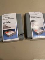 Two folded Room Essentials underbed storage organizers with packaging labels visible on top, placed side by side on a flat surface.