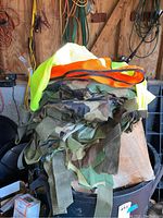 Photo of assorted army camouflage fabric scraps with straps, with neon yellow and orange reflector vests on top