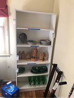 Front view of white bookcase filled with plates, figurines and green glassware.