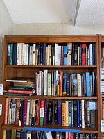Three wooden shelves packed with numerous hardback and paperback books on history topics.